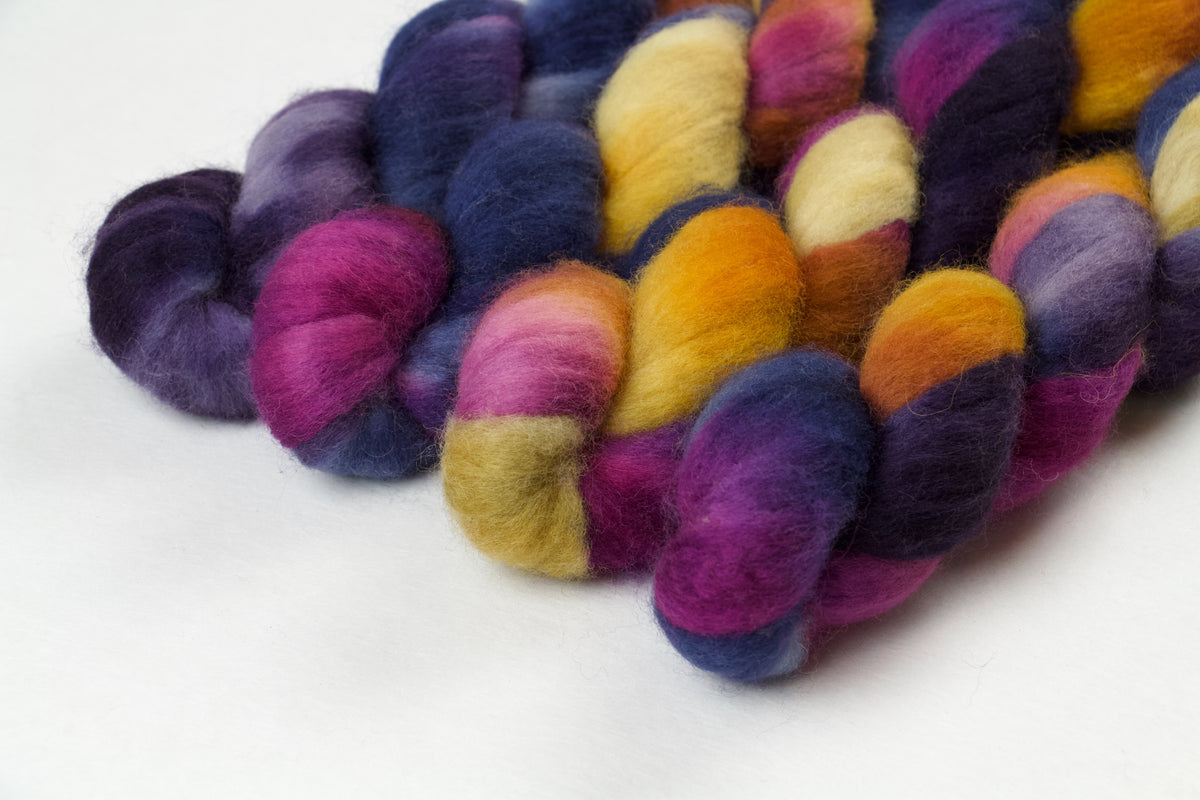 Braided fiber skein with blue, purple, pink, and gold on a white background