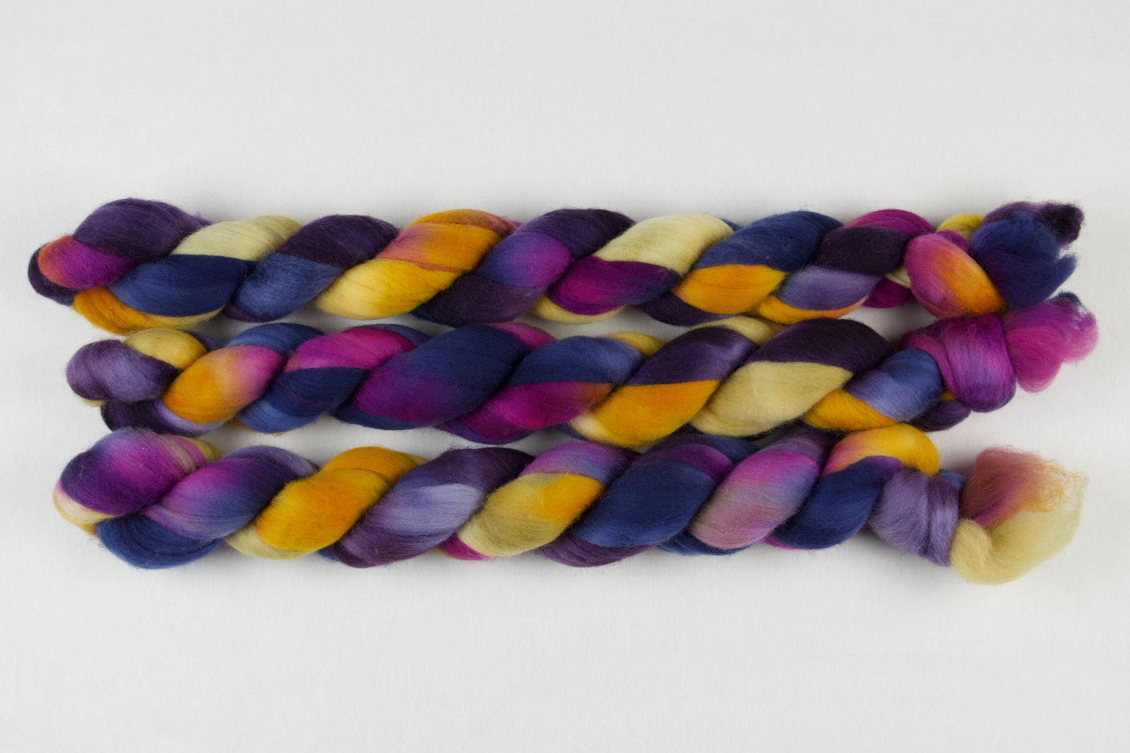 Braided fiber skein with blue, purple, pink, mustard, and gold on a white background