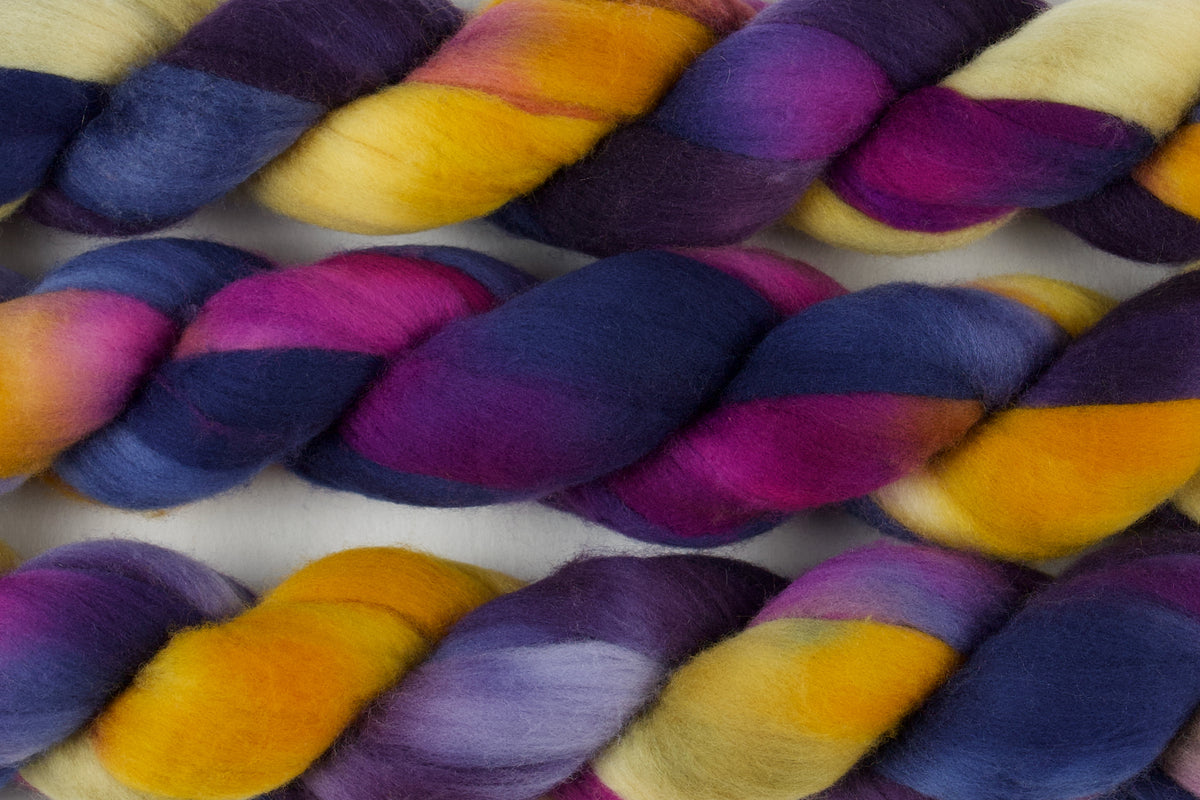 Braided fiber skein with blue, purple, pink, mustard, and gold on a white background