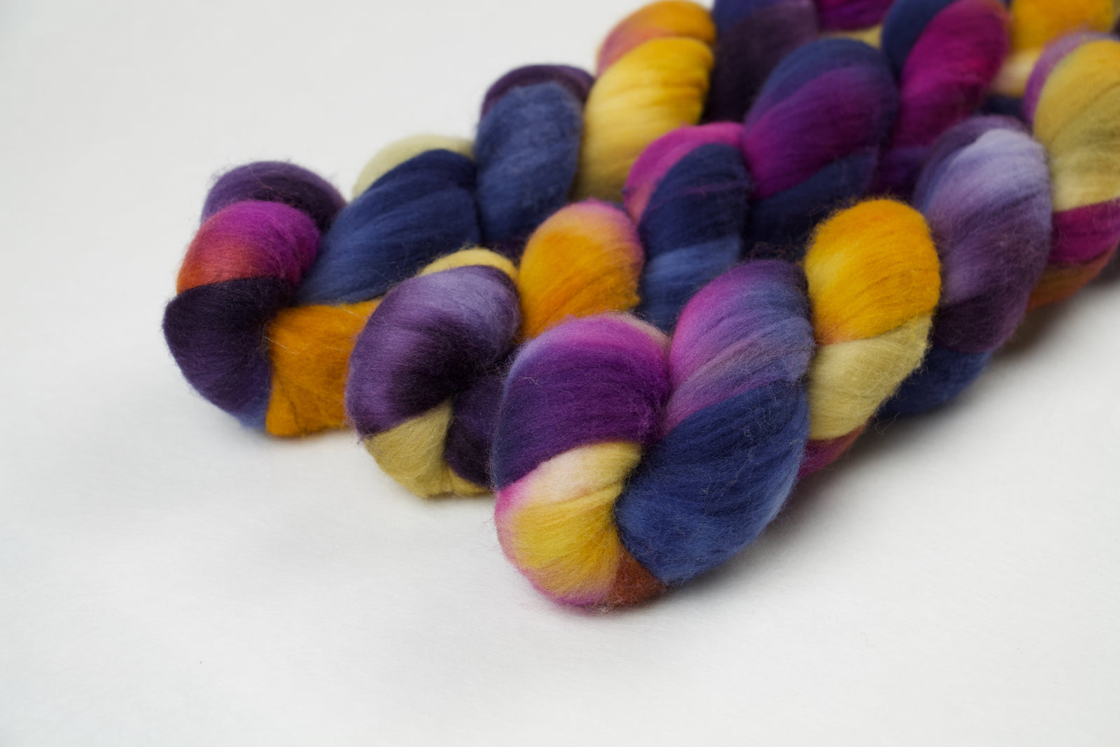 Braided fiber skein with blue, purple, pink, mustard, and gold on a white background