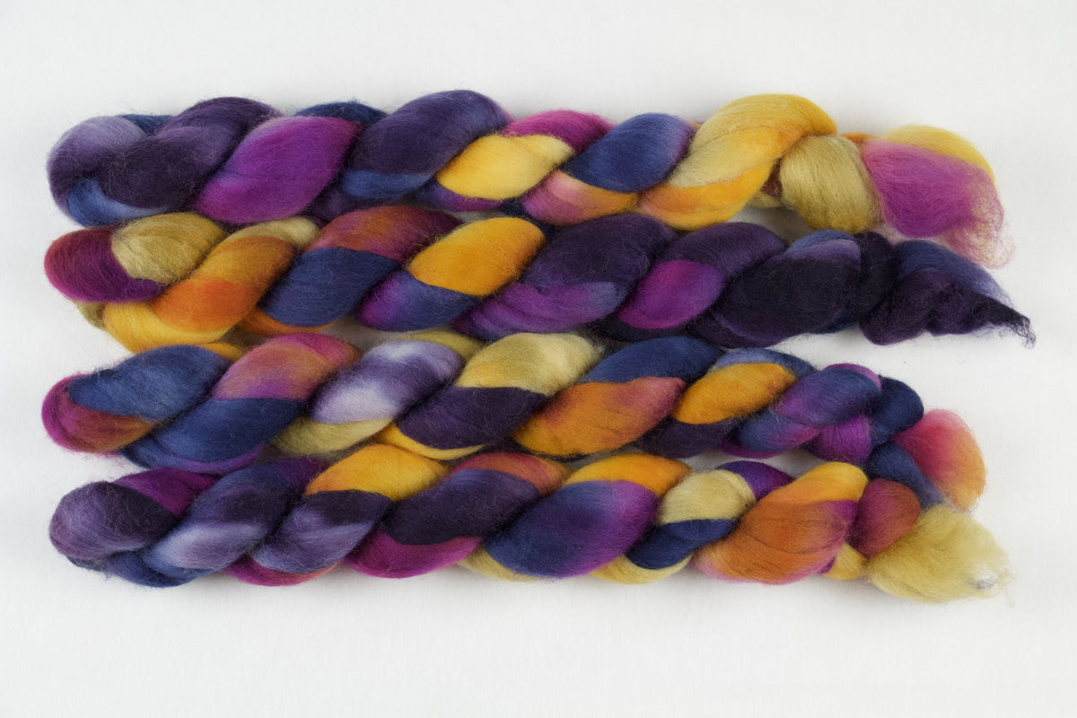 Braided fiber skein with blue, purple, pink, and gold on a white background