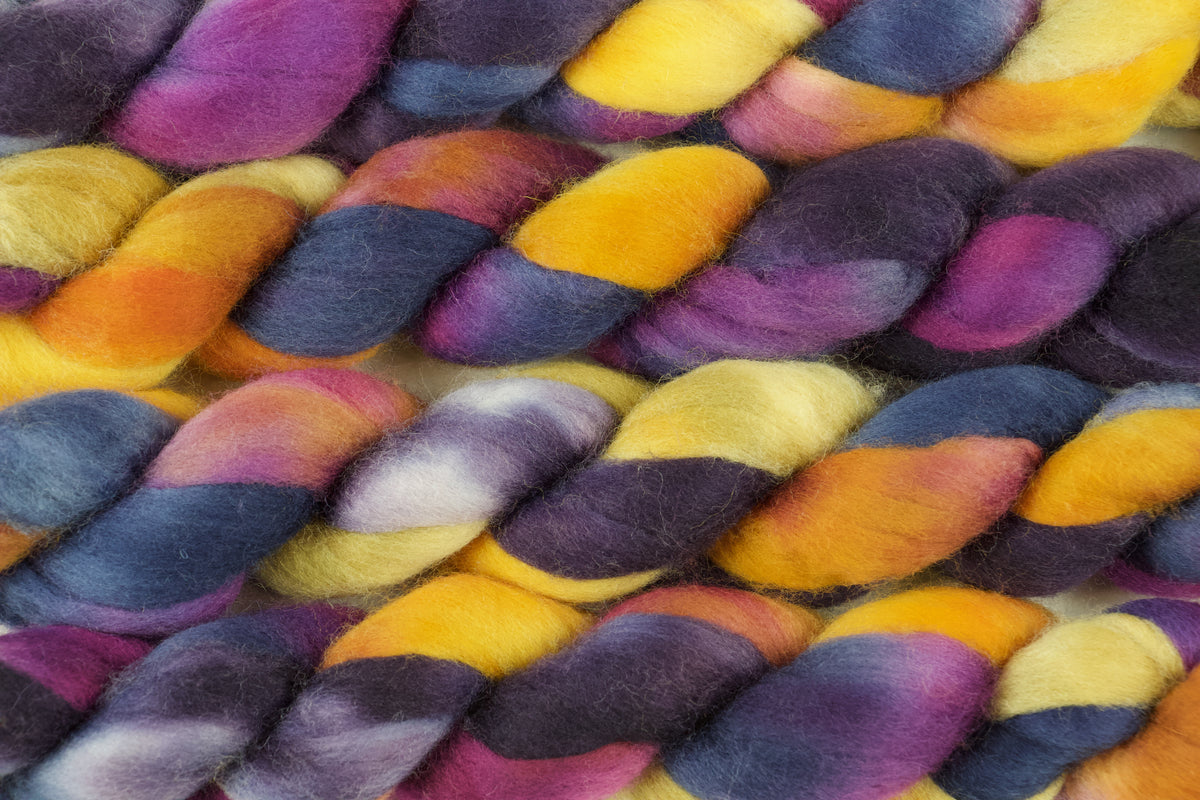 Braided fiber skein with blue, purple, pink, and gold on a white background