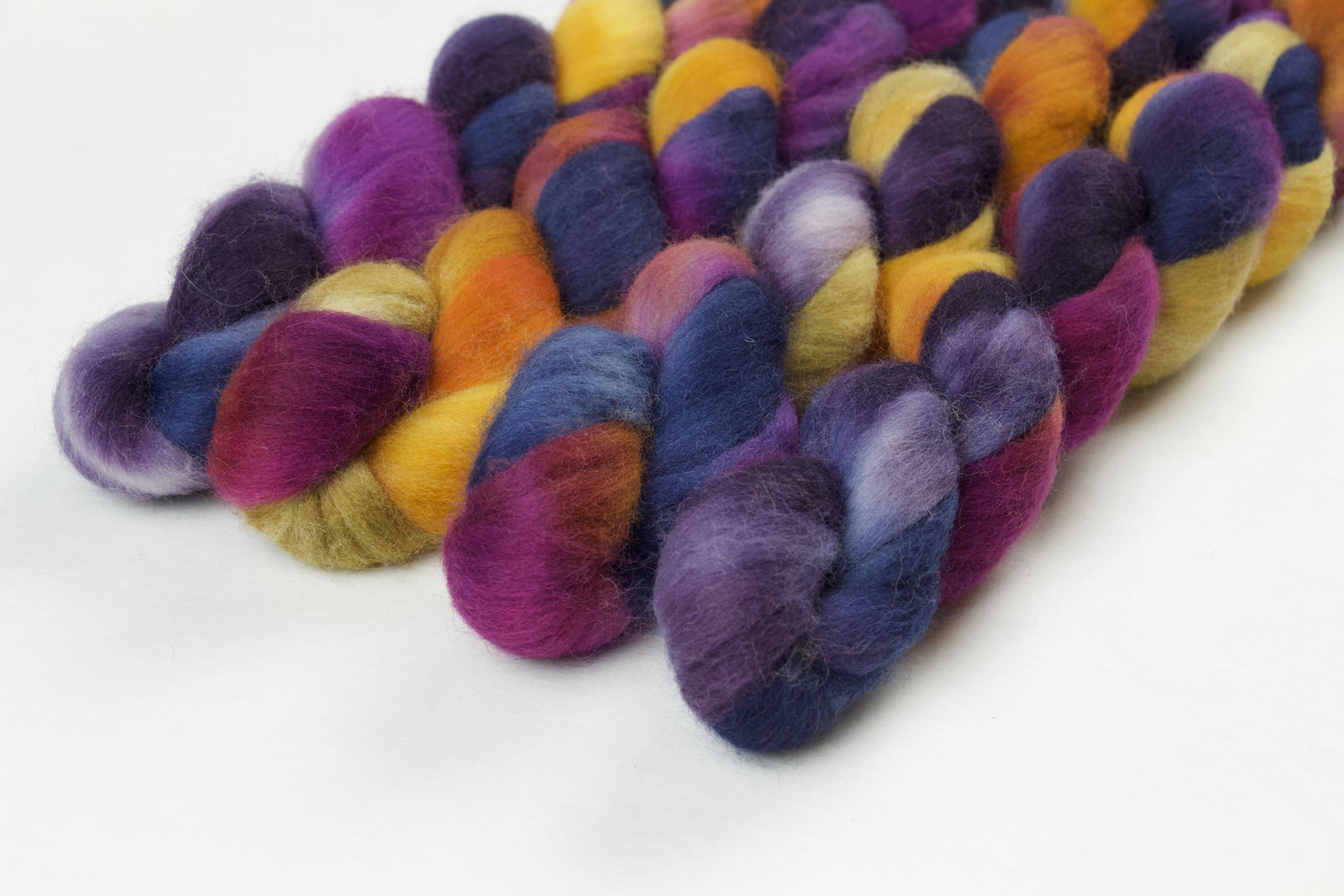 Braided fiber skein with blue, purple, pink, and gold on a white background