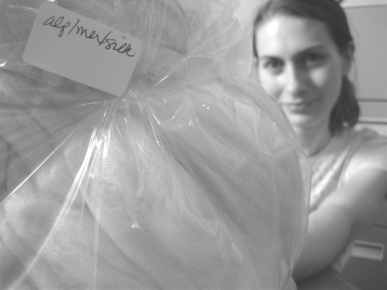 Person holding a large wrapped item with a label, in black and white.
